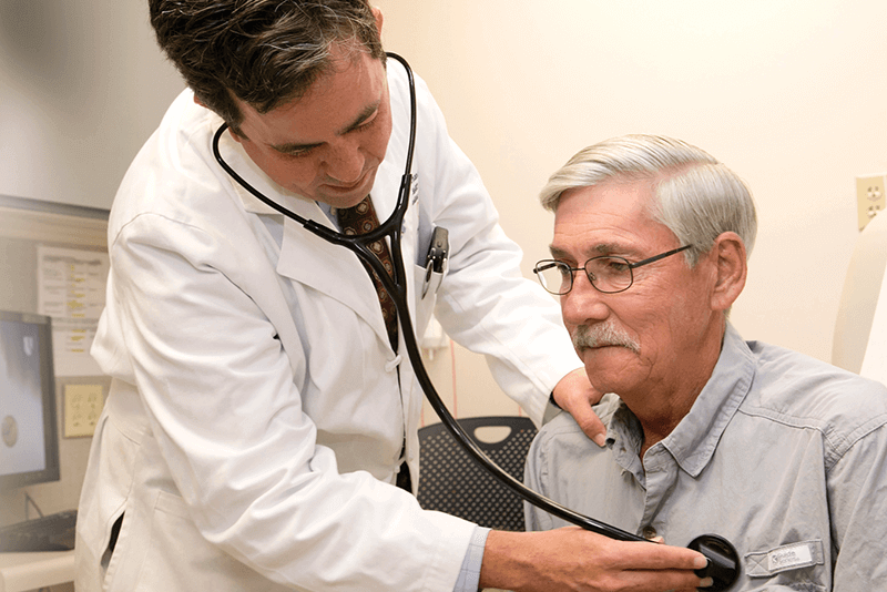 A doctor uses a stethoscope to listen to an elderly gentleman's heart.