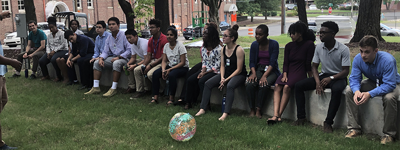 Multiple STAR Program students are seen sitting on a brick wall outside with an inflatable ball in front of them preparing for a fun team building exercise.