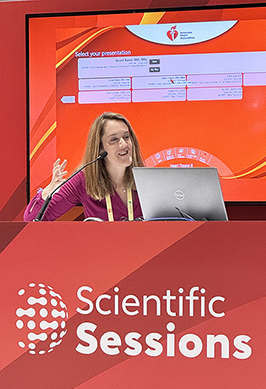 DCRI's Jennifer Rymer sits at a red panel table with the 2024 AHA Scientific Sessions logo on the front of it. She speaks in an animated nature while discussing best practices.