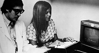 Historical, black and white image from the early 1970s showing a man and a woman performing data entry.