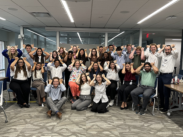 STAR program participants and staff gather in a conference room for a group photo. The group is posed together and making matching hand gestures known as the Durham "bull horns.".