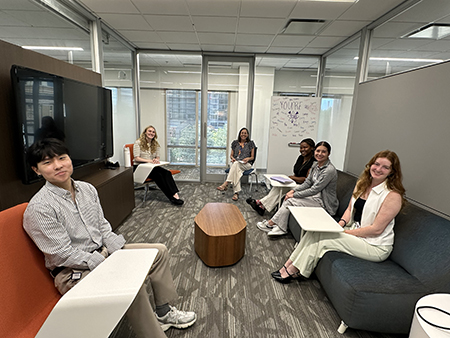 Six STAR Program participants are seated in a glass-walled meeting area furnished with lounge seating and small tables. The group is gathered for discussion as part of a collaborative learning activity.