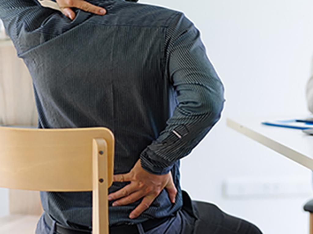 A person facing away from the camera holds the back of their neck and their low back with each hand. 