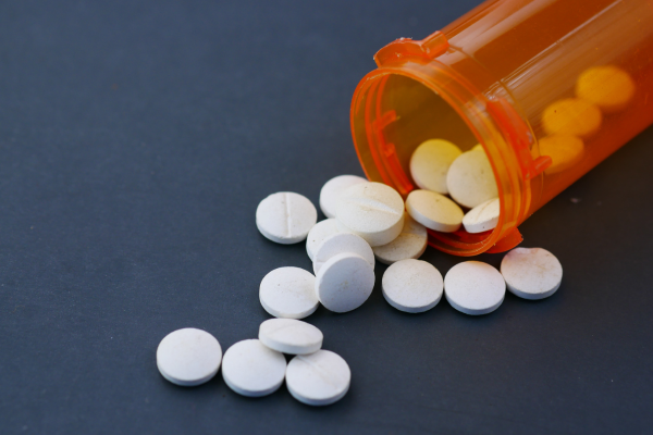 White, round pills spill out of an orange pill bottle against a slate color background.