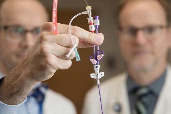 Two doctors hold up a piccline to the camera as they examine it.