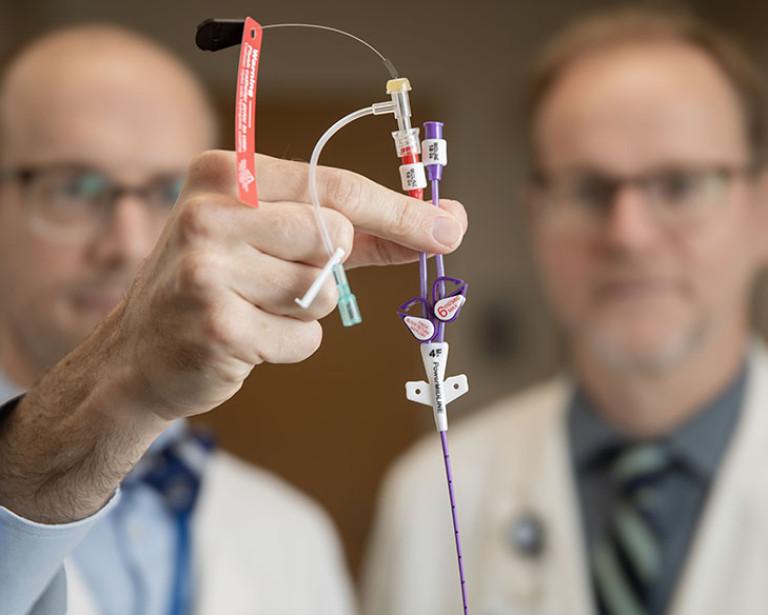 Two doctors hold up a piccline to the camera as they examine it.