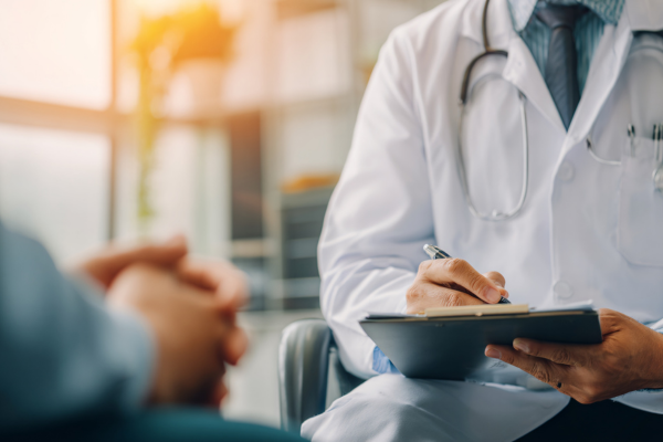 A doctor references their clipboard of notes as they consult with a patient in a brightly lit room.