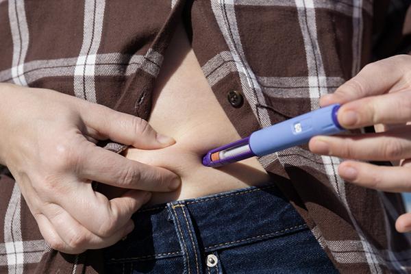 Insulin injection pen semaglutide medication blue medical device of slim woman injecting abdomen with glp 1 diabetes treatment at home.