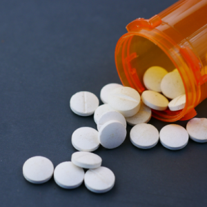 White, round pills spill out of an orange pill bottle against a slate color background.