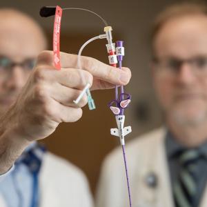 Two doctors hold up a piccline to the camera as they examine it.